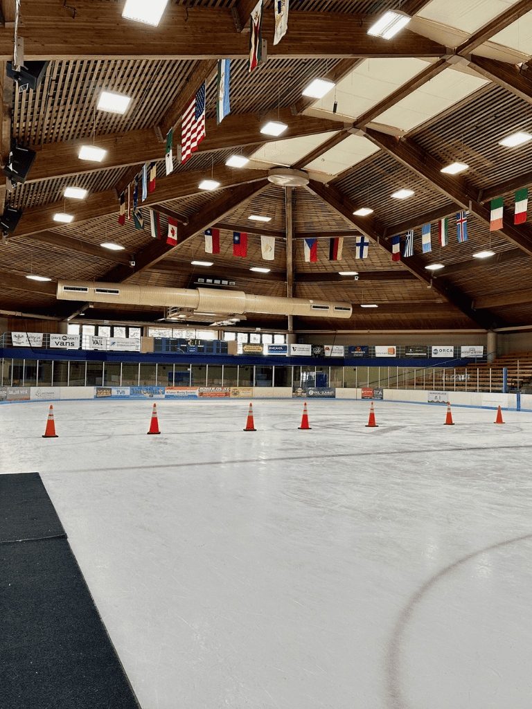 Ice rink with flags hanging from the wooden ceiling at QuestForDirections sports facility.