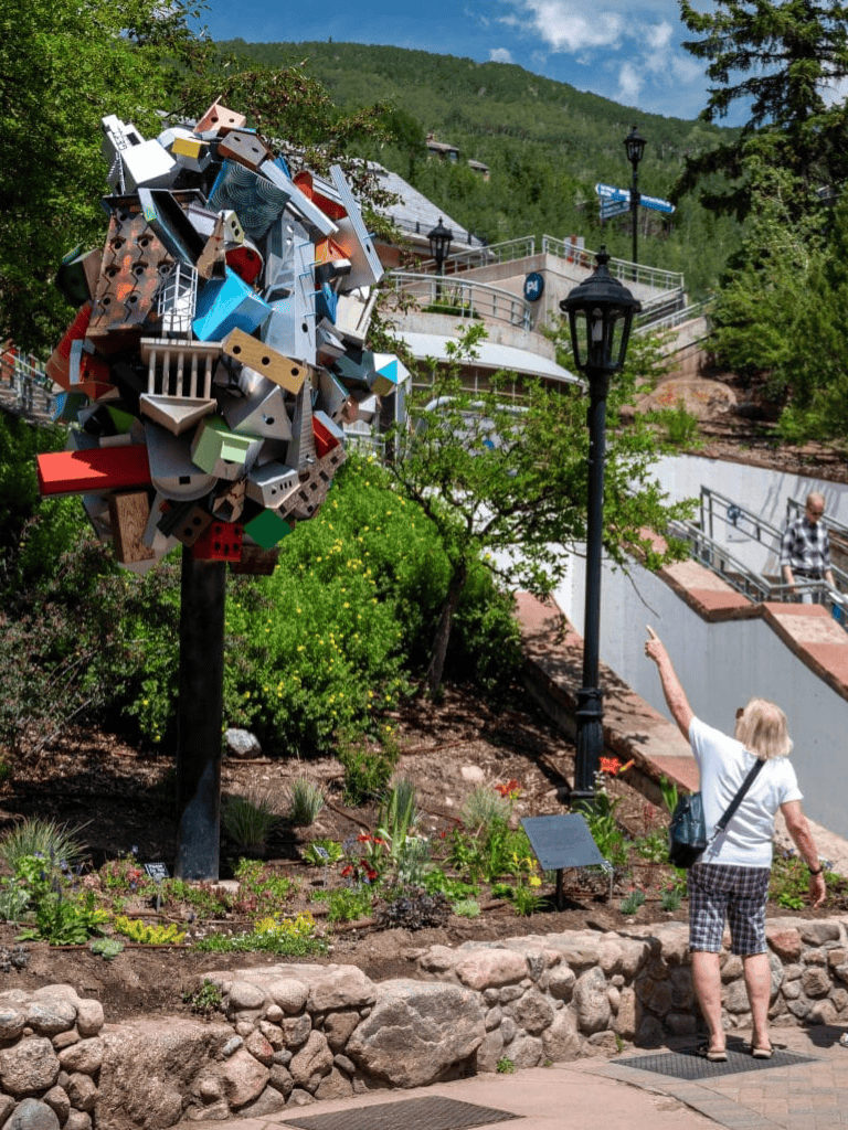 Colorful abstract outdoor sculpture in a scenic mountain town, surrounded by greenery and historic street lamps.