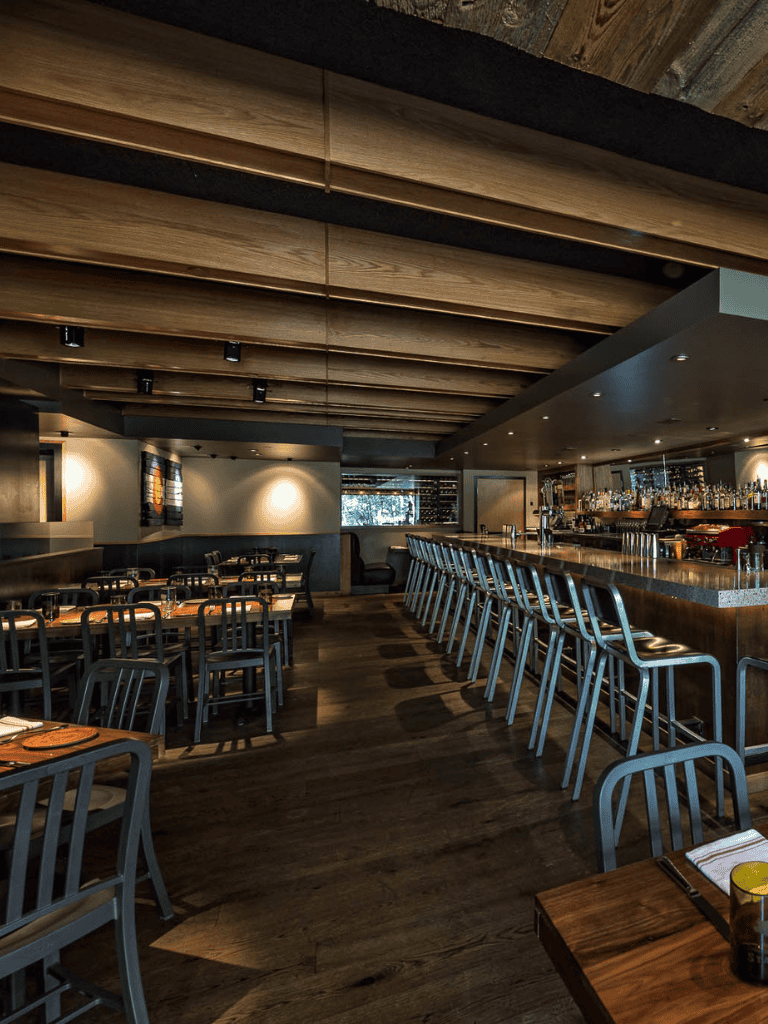 Cozy modern restaurant interior with bar seating, wooden accents, and ambient lighting, perfect for dining and socializing.