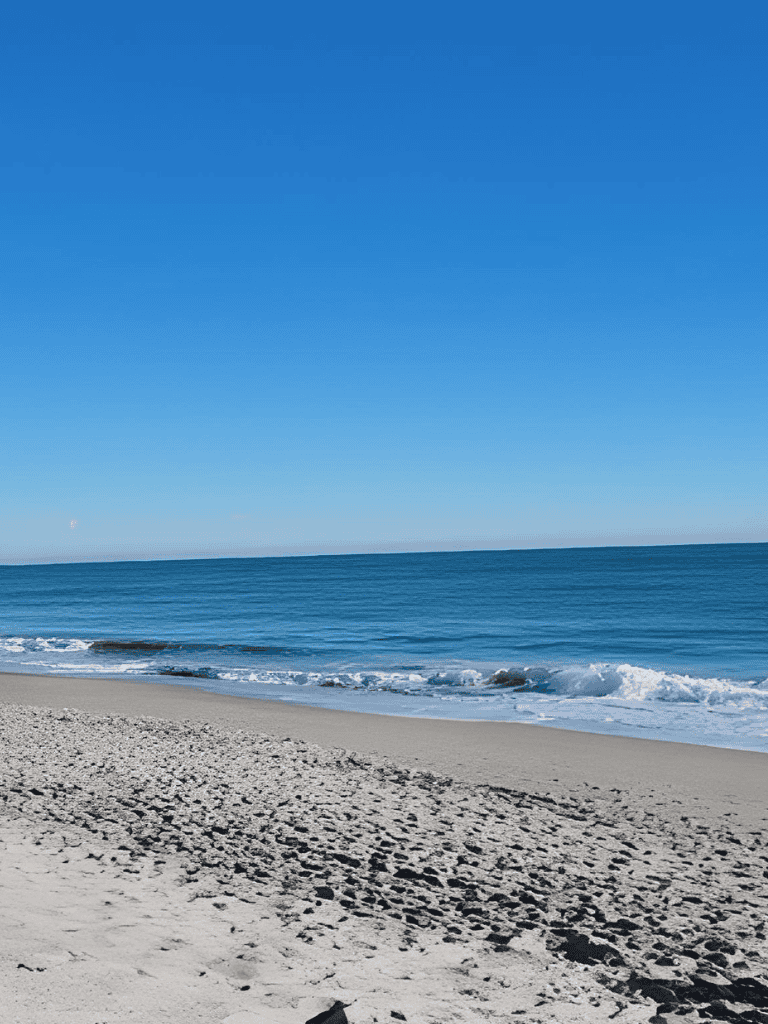 Sunny beach with clear blue sky and calm ocean waves during daytime.