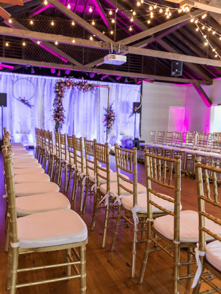 Elegantly decorated wedding ceremony setup with gold Chiavari chairs, floral arrangements, and string lights.