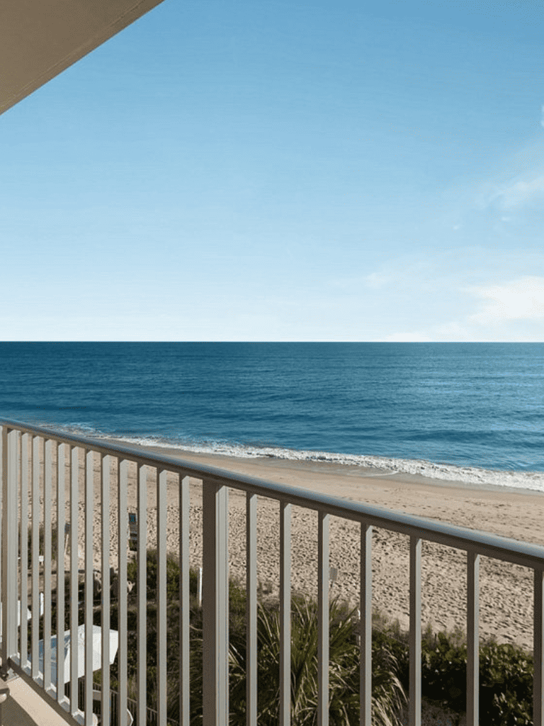Breathtaking ocean view from balcony overlooking sandy beach and clear blue sea.
