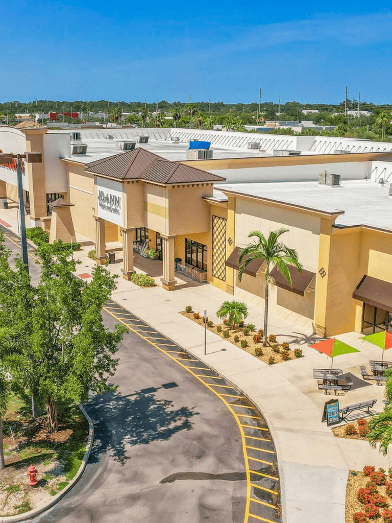 Exterior shopping mall with palm trees and outdoor seating for dining and browsing.