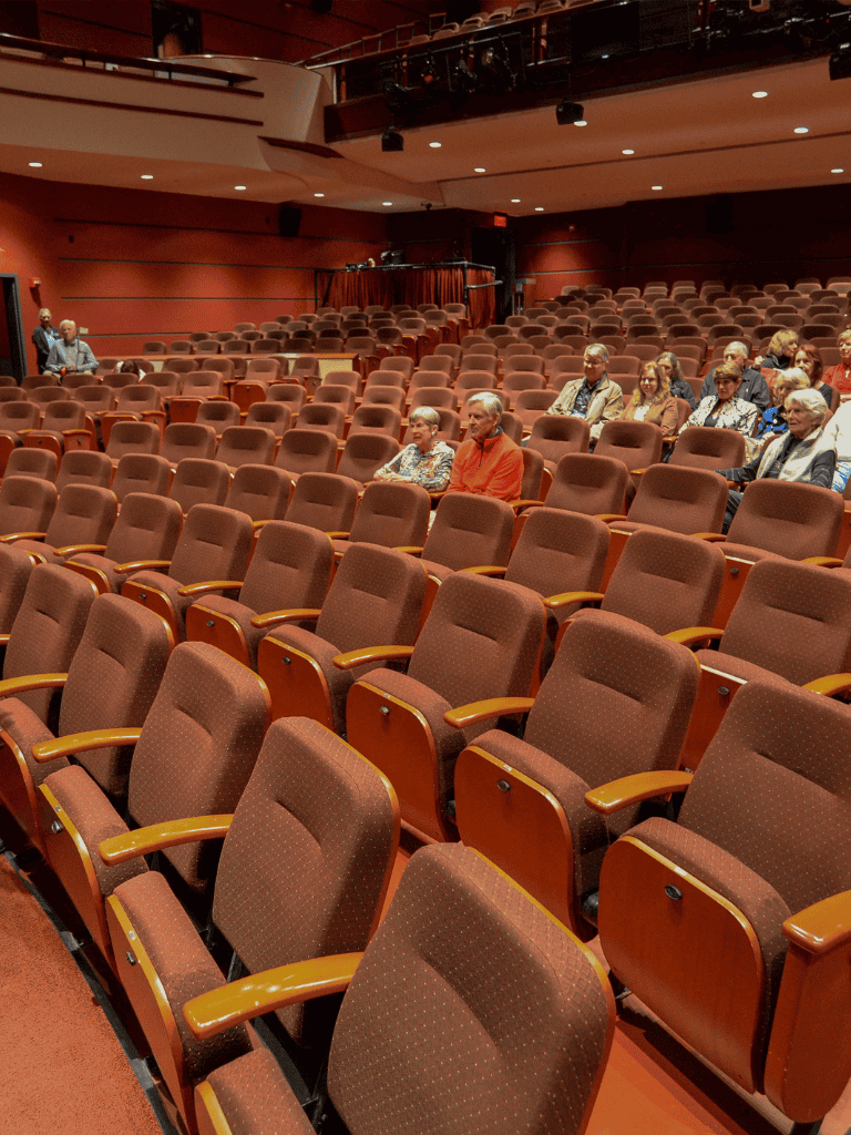 Quiet auditorium with brown cushioned seats and audience members waiting for a performance.