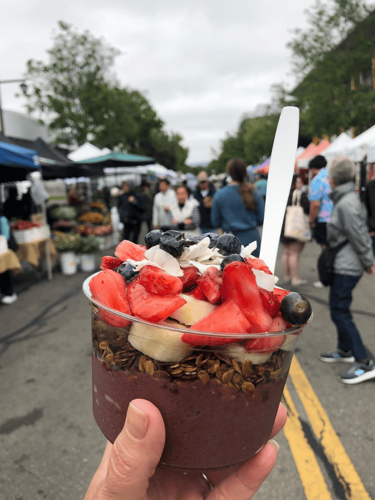 Fresh berry parfait with granola at outdoor farmers market, healthy dessert option.