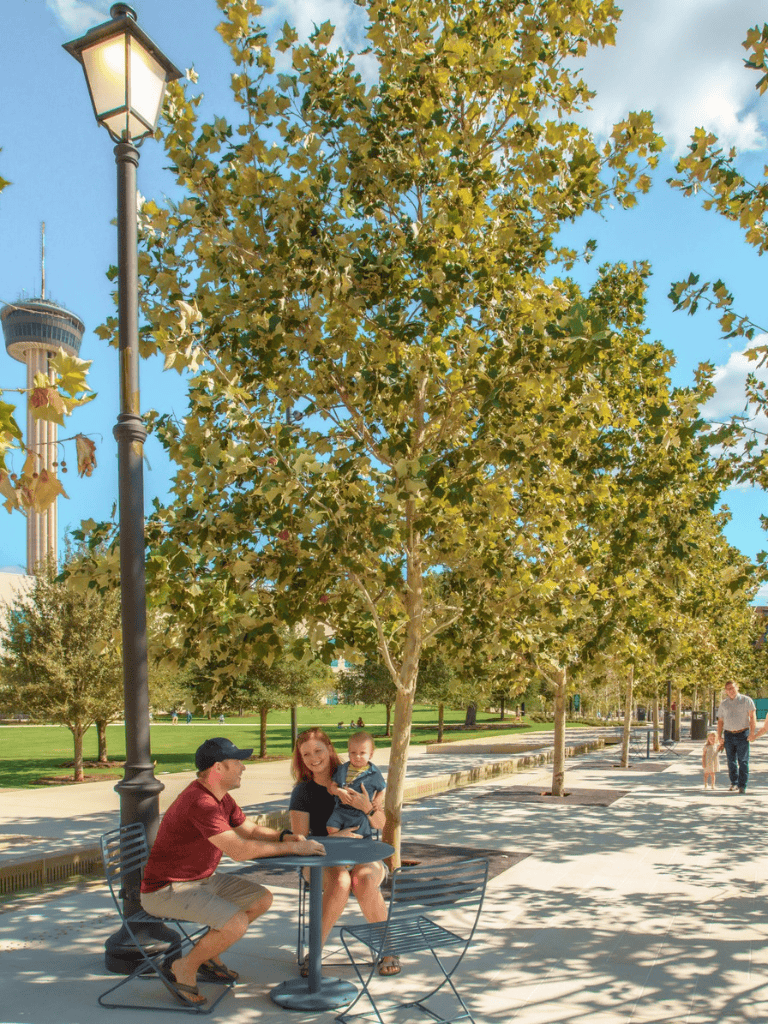 Relaxing park scene with family enjoying outdoors, trees, and city skyline in background.