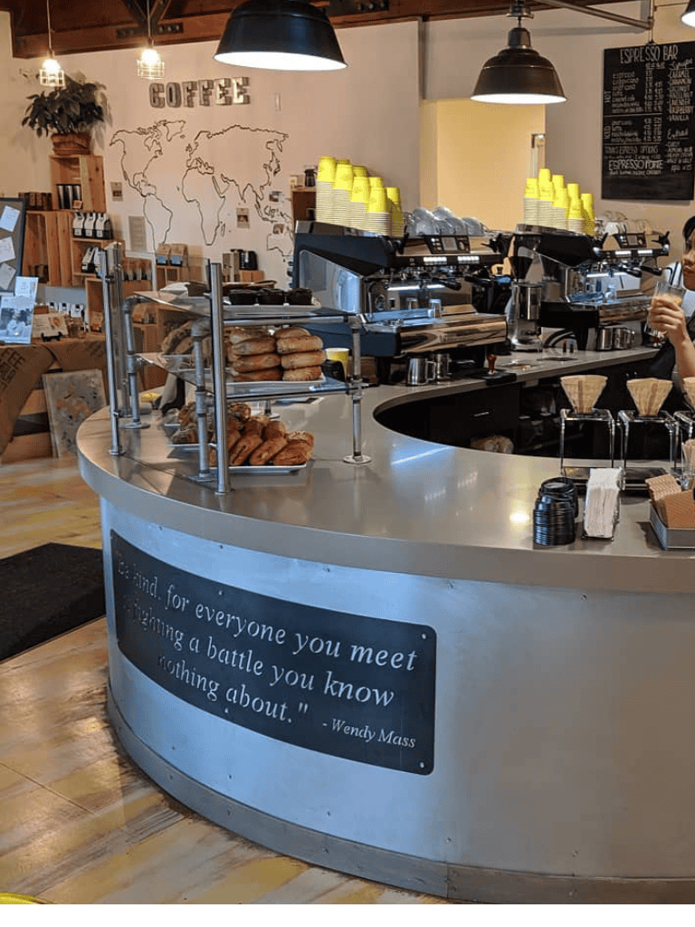 Coffee shop interior with bakery display and espresso machines.