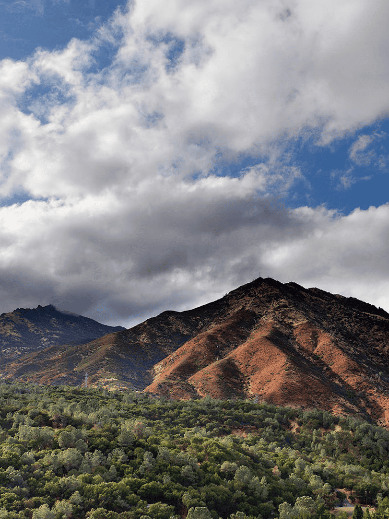 Vast mountain landscape with rugged terrain and lush green foliage under cloudy sky.