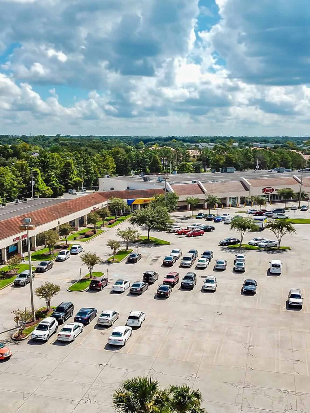 Empty shopping plaza parking lot with retail stores and a wide sky view, ideal for local shopping and dining.