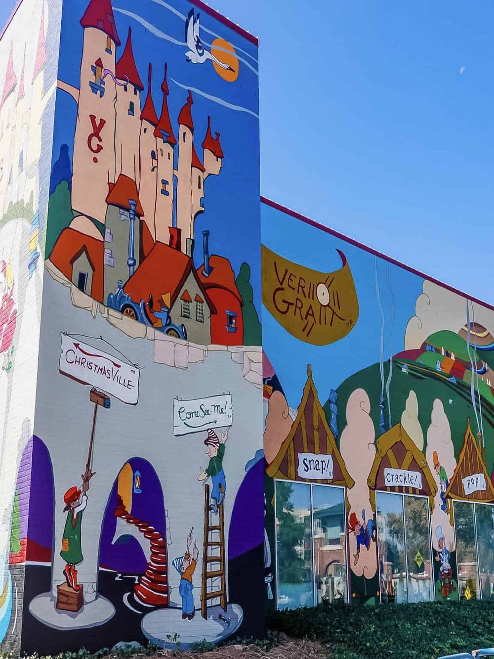 Colorful mural depicting whimsical castles, characters, and playful scenes in a vibrant outdoor setting.