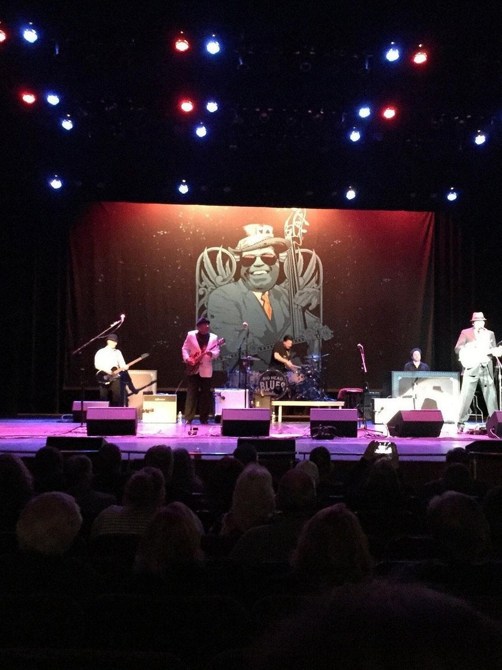 Vintage blues band performing live on stage with colorful lights and animated backdrop.