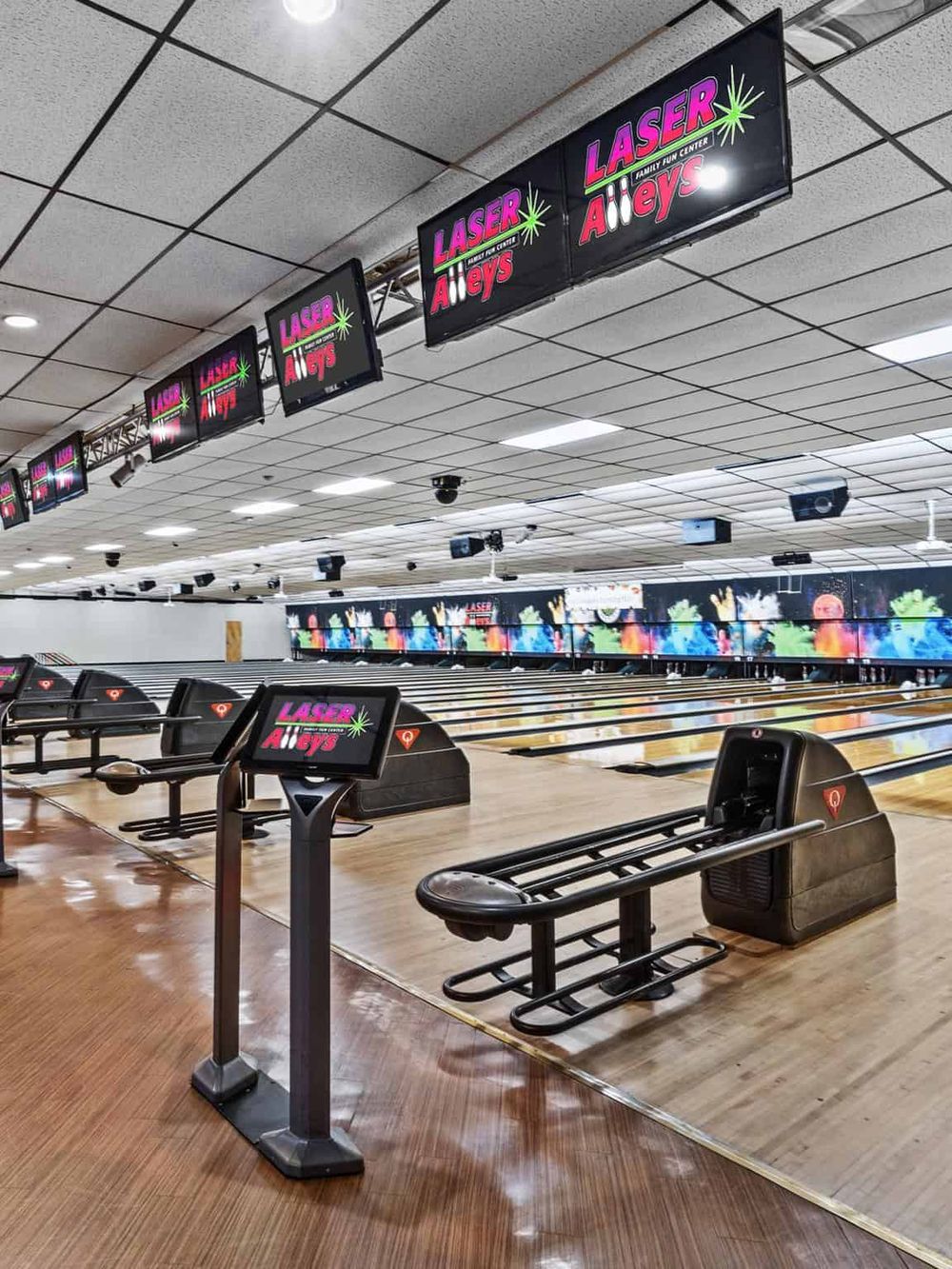 Bright laser alley at bowling center with multiple lanes and electronic score screens.