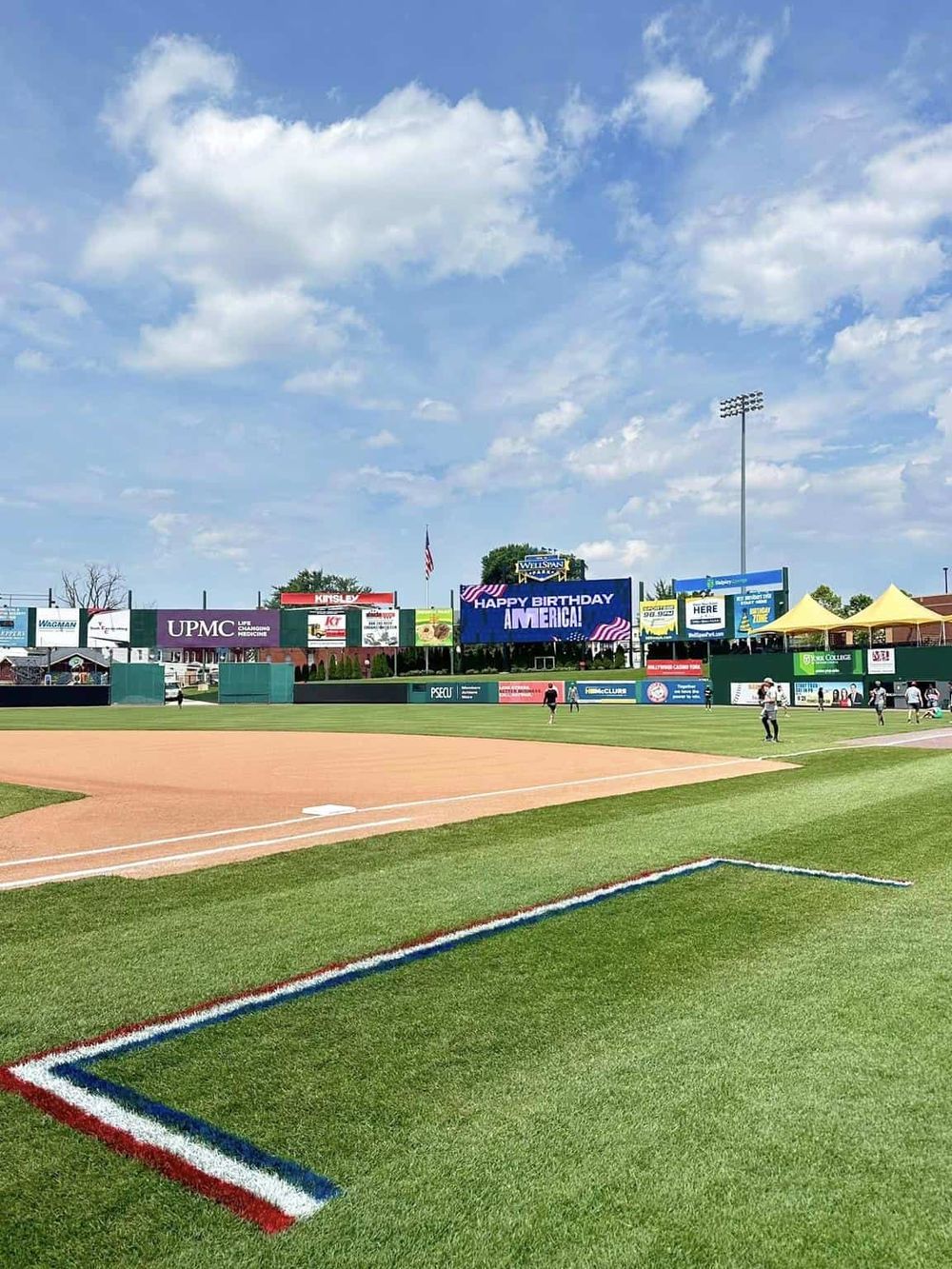 Baseball stadium with digital scoreboard and players, vibrant green field, festive atmosphere.