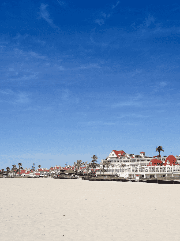 Tropical beach resort with white sandy shoreline and red-roofed buildings under blue sky.