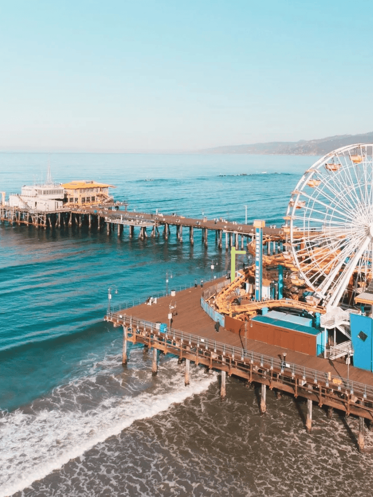 Brightly lit Santa Monica Pier with ocean views and Ferris wheel near the beach, popular California tourist destination.