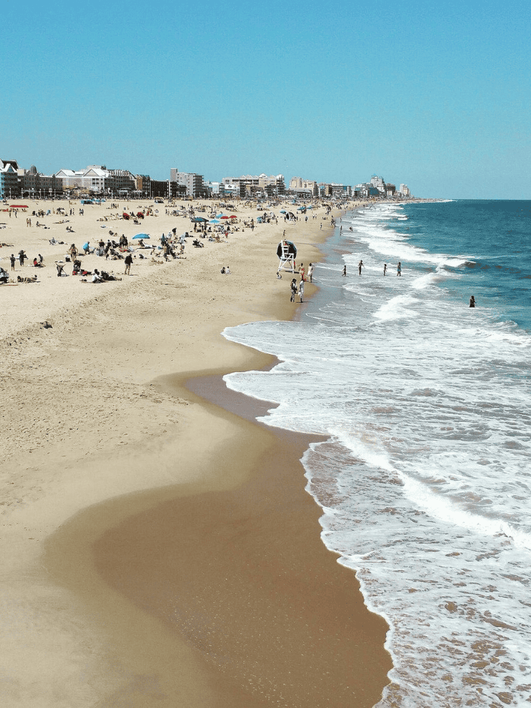 Sunny beach with people relaxing and playing, coastal town skyline in the background, ideal for travel and vacation planning.