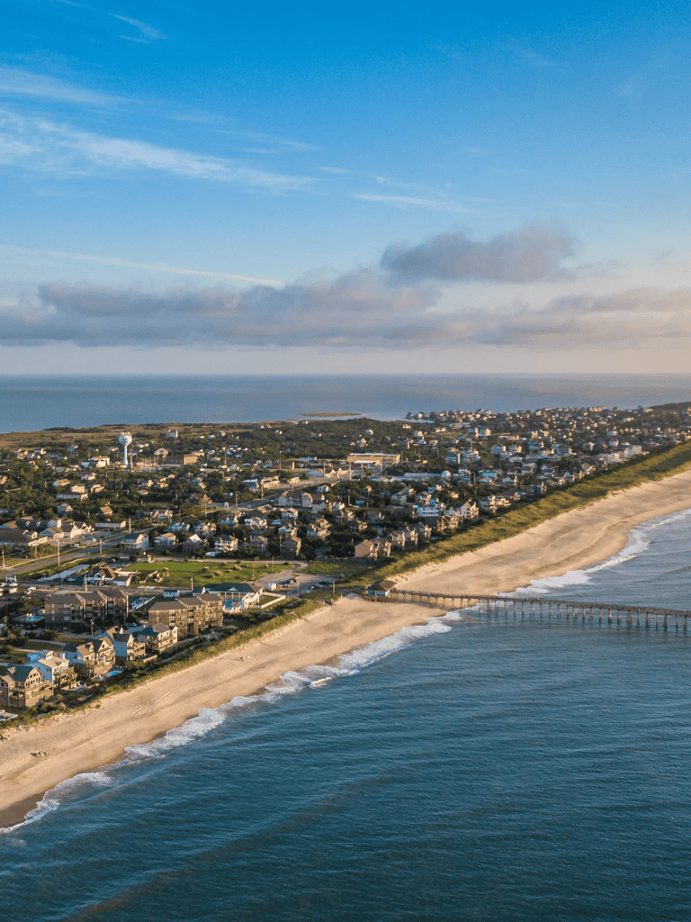 Aerial view of a coastal town with beach, pier, and ocean scenery at sunset.