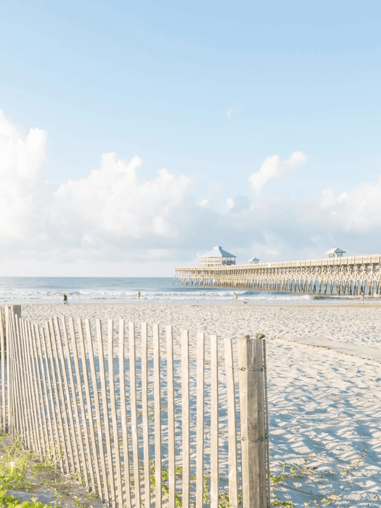 Bright sunny beach scene with a pier and wooden fence, ideal for seaside and vacation travel keywords.