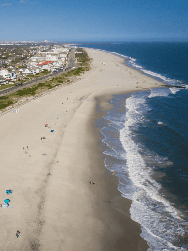 Aerial view of a sunny beach with umbrellas, shoreline, and nearby coastal town.