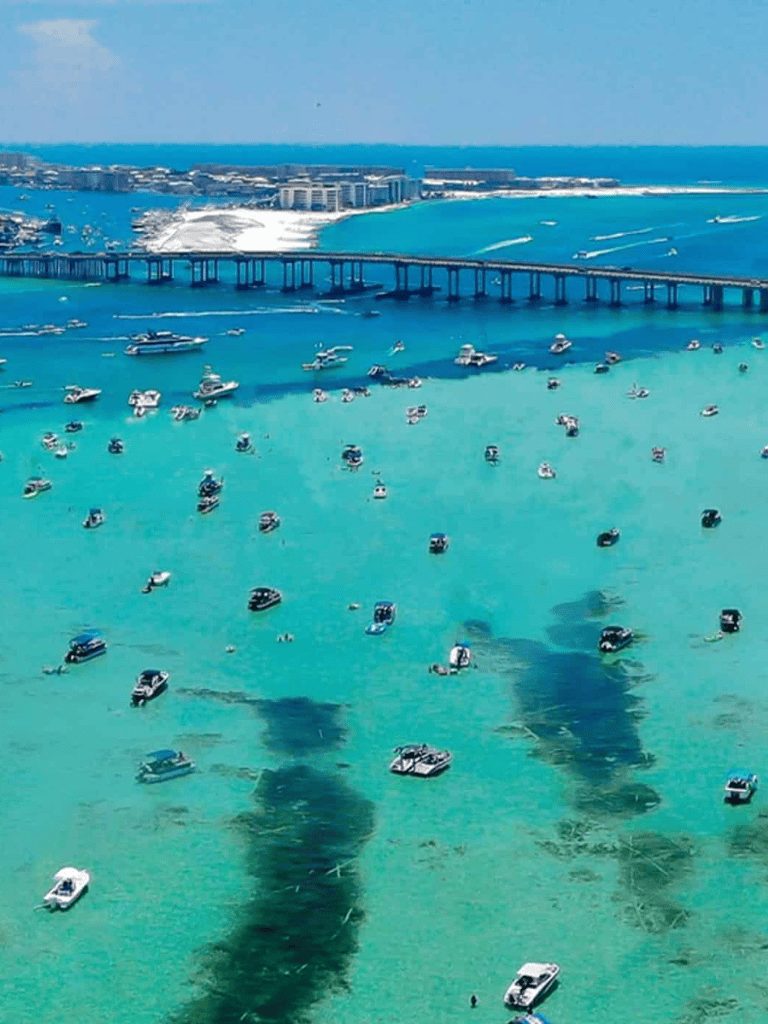 Boats in turquoise water with a bridge and cityscape in the background, scenic coastal travel destination.