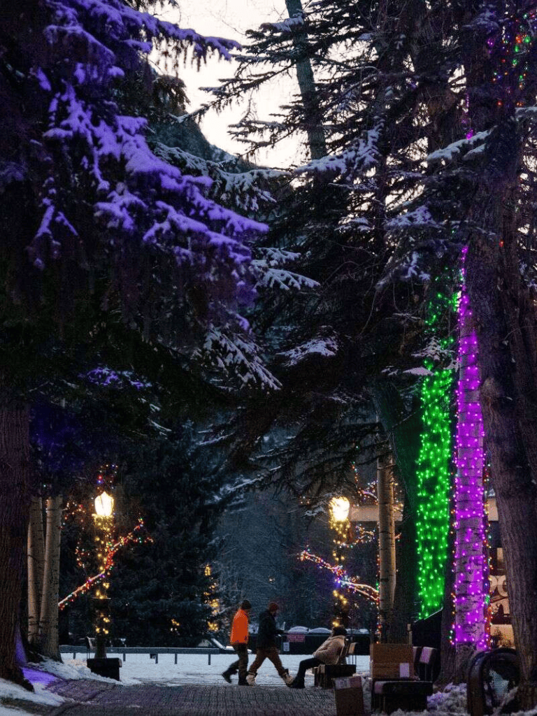 Colorful holiday lights illuminating a snowy park with people walking and enjoying the winter evening.