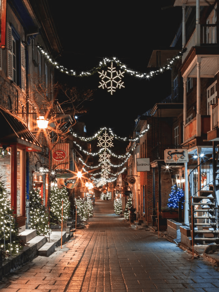 Festive holiday street decorated with snowflake string lights and illuminated storefronts, capturing a charming winter evening scene.