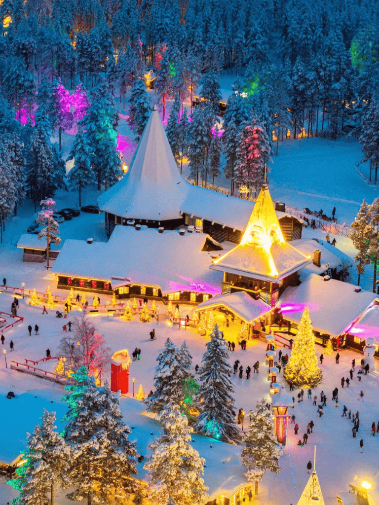 Colorfully illuminated winter village with Christmas trees and snow-covered buildings at night.