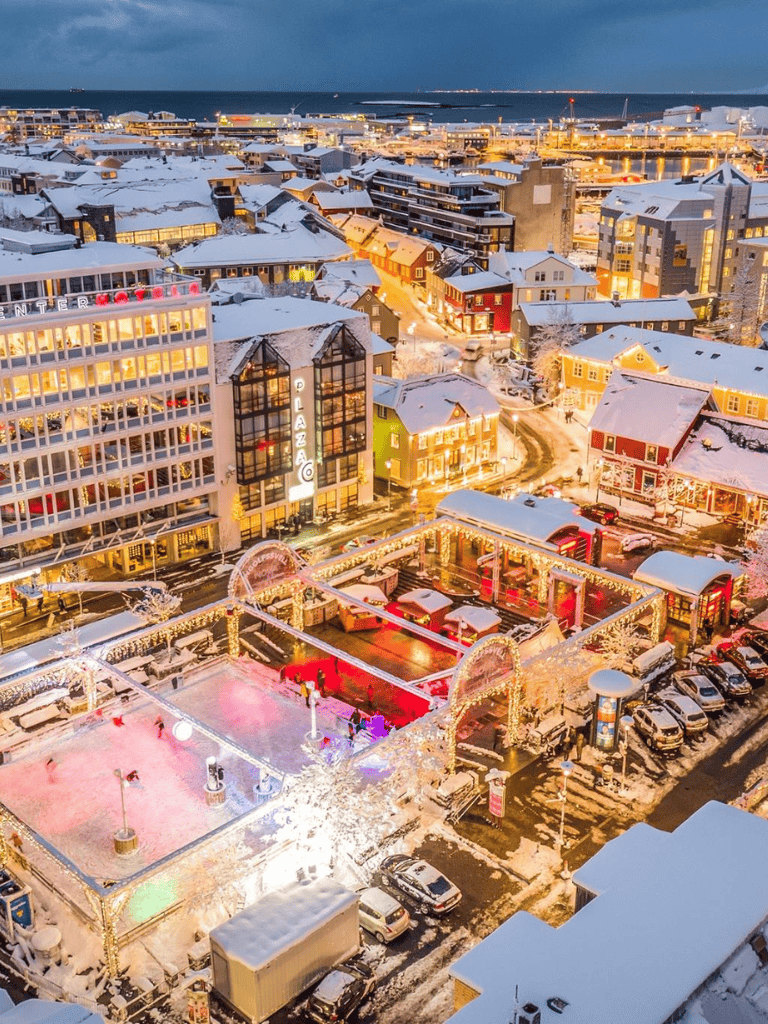 Snowy waterfront cityscape with illuminated buildings and outdoor skating rink, showcasing a vibrant urban winter scene.