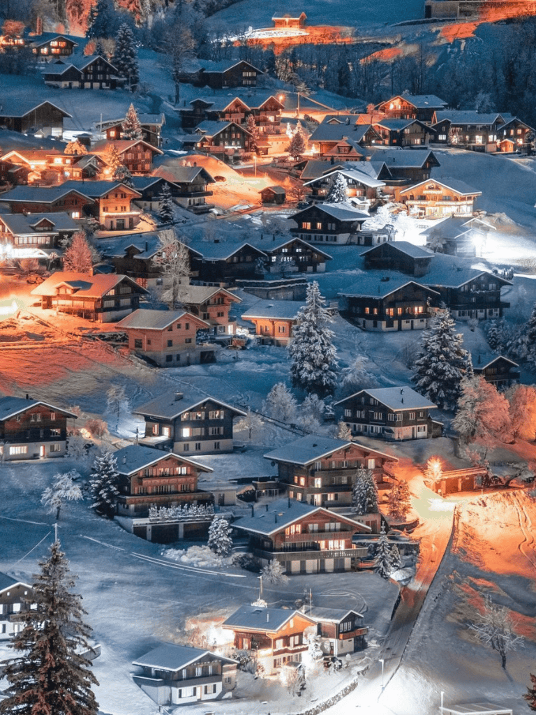 Snowy mountain village with illuminated chalets and winter landscape.