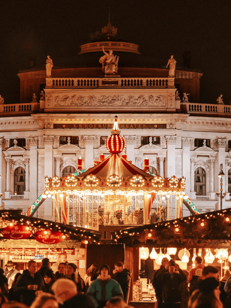 Colorful carousel at night outside historic building, festive holiday atmosphere with cheerful crowd.