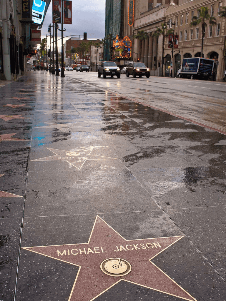Pink star on Hollywood Walk of Fame honoring Michael Jackson, city street scene, rainy weather.