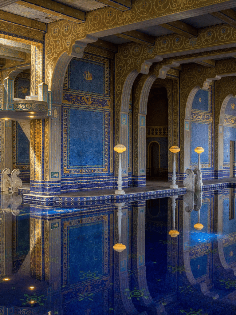 Ornate interior of a historic palace with gold accents and blue mosaic tiles reflecting in a pool.