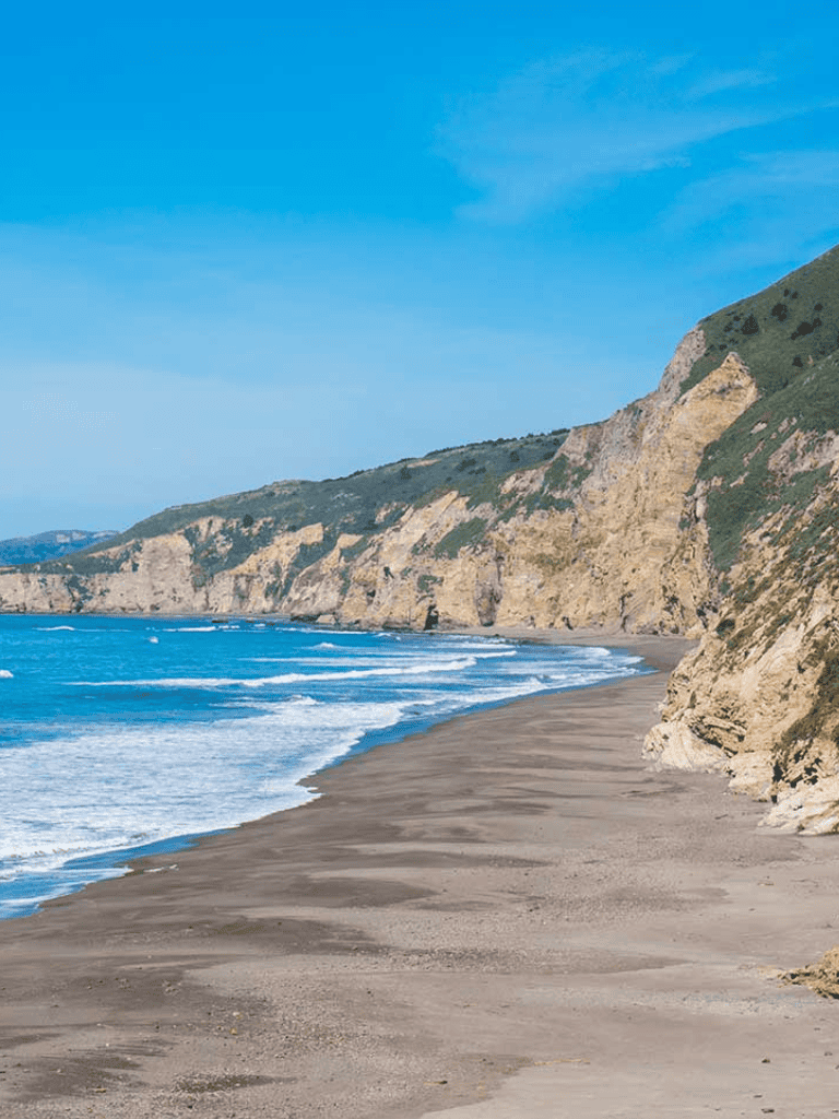 Tranquil beach with cliffs and blue ocean waves, perfect for coastal adventures and scenic drives.