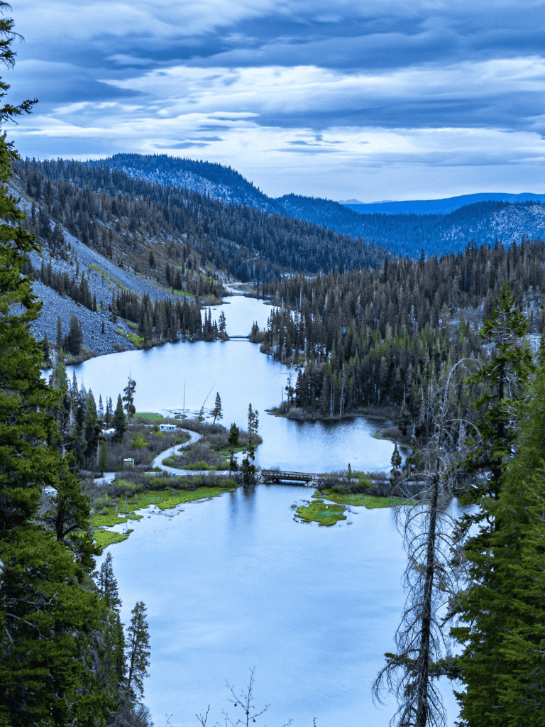 Serene mountain lake surrounded by lush forest and dramatic skies, scenic outdoor adventure destination.