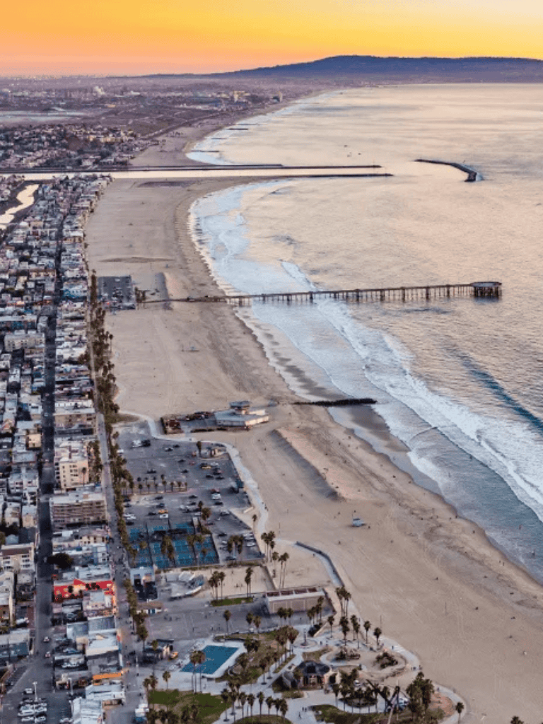 Sunset view of Huntington Beach, California with sandy shoreline, pier, and ocean waves.