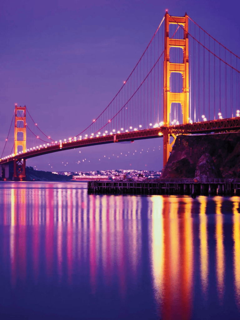 Golden Gate Bridge at night illuminated with vibrant lights, reflecting in the San Francisco Bay.