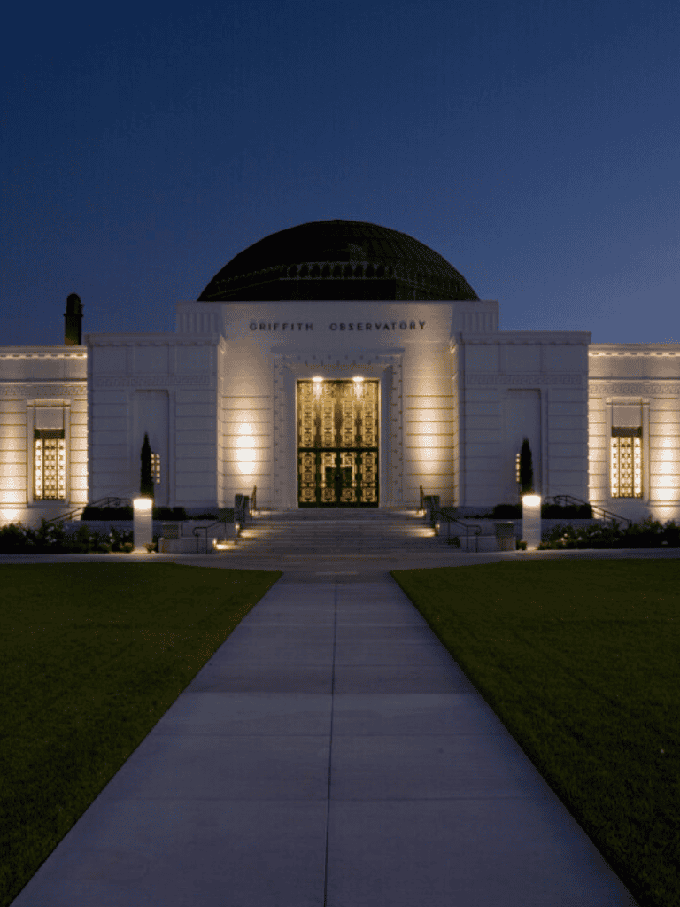 Modern Griffith Observatory at night with illuminated entrance, iconic architecture, and surrounding pathways.