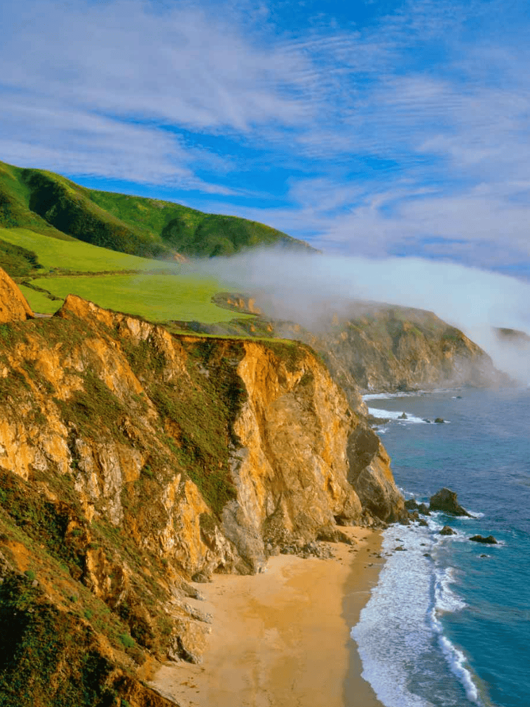Breathtaking coastal cliffs with lush greenery overlooking a sandy beach and the Pacific Ocean.