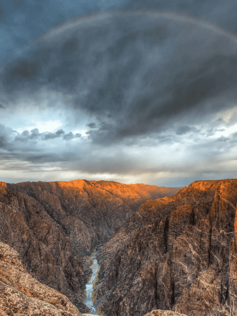 Rugged canyon with a winding river and dramatic storm clouds, showcasing natural adventure at QuestForDirections.