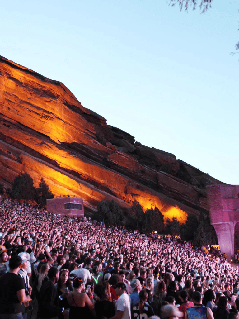 Vivid outdoor concert with a large audience at Red Rocks Amphitheatre, illuminated rock formations.