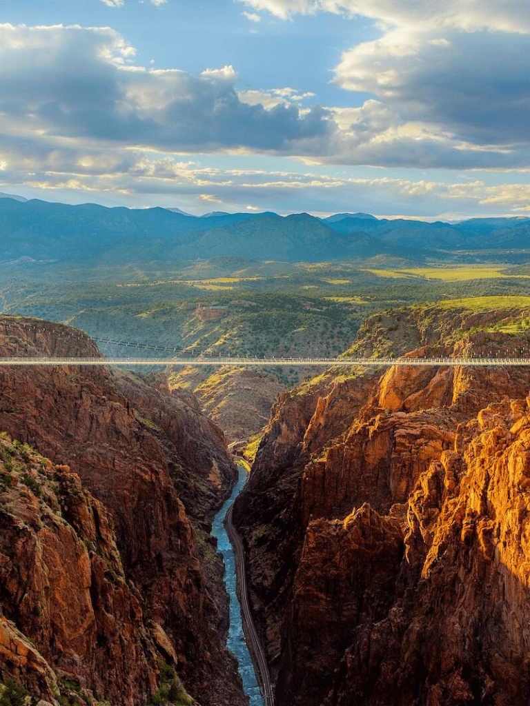 Breathtaking view of the Grand Canyon with a suspension bridge and Colorado River at sunset, showcasing natural scenic beauty.