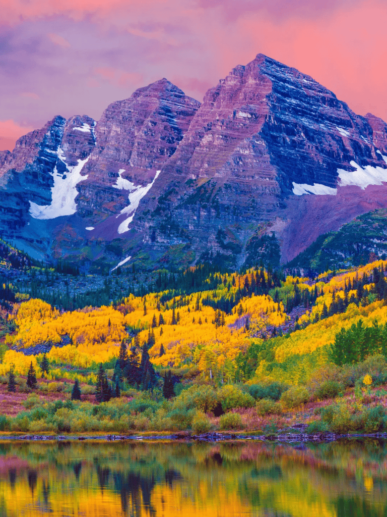 Vibrant autumn landscape with mountains, colorful trees, and calm lake reflection in the Rockies.