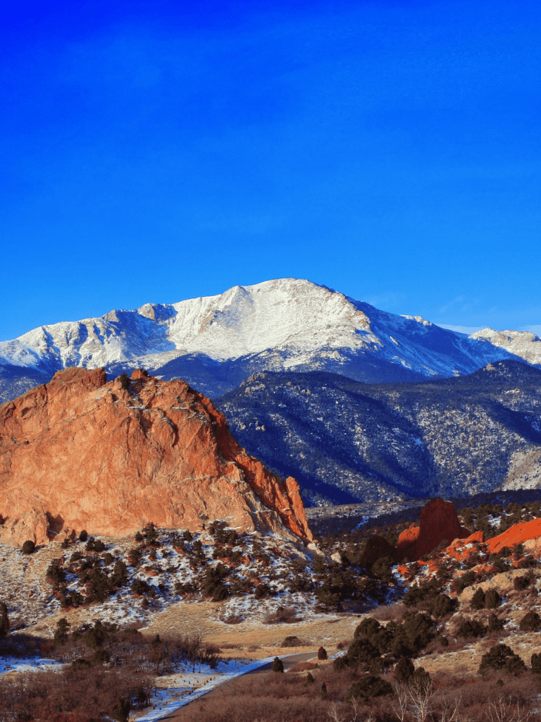 Snow-capped mountains with red rocks and a clear blue sky in Colorado.