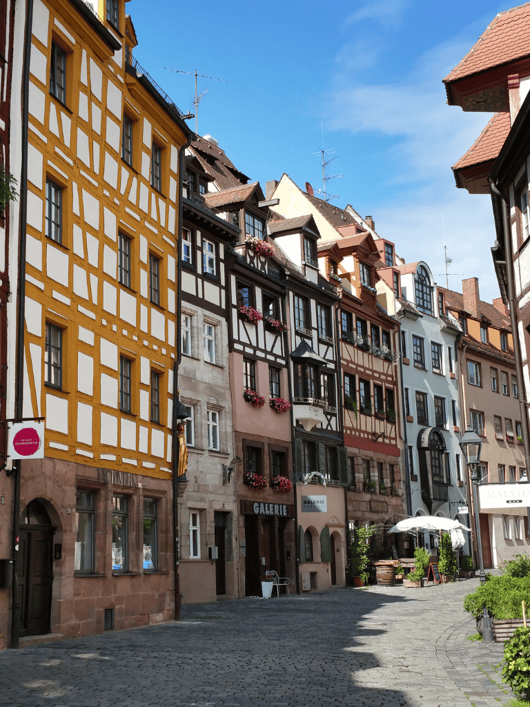 Colorful European townhouses with flower boxes on windows, cobblestone street, and boutique galleries in a scenic historic district.