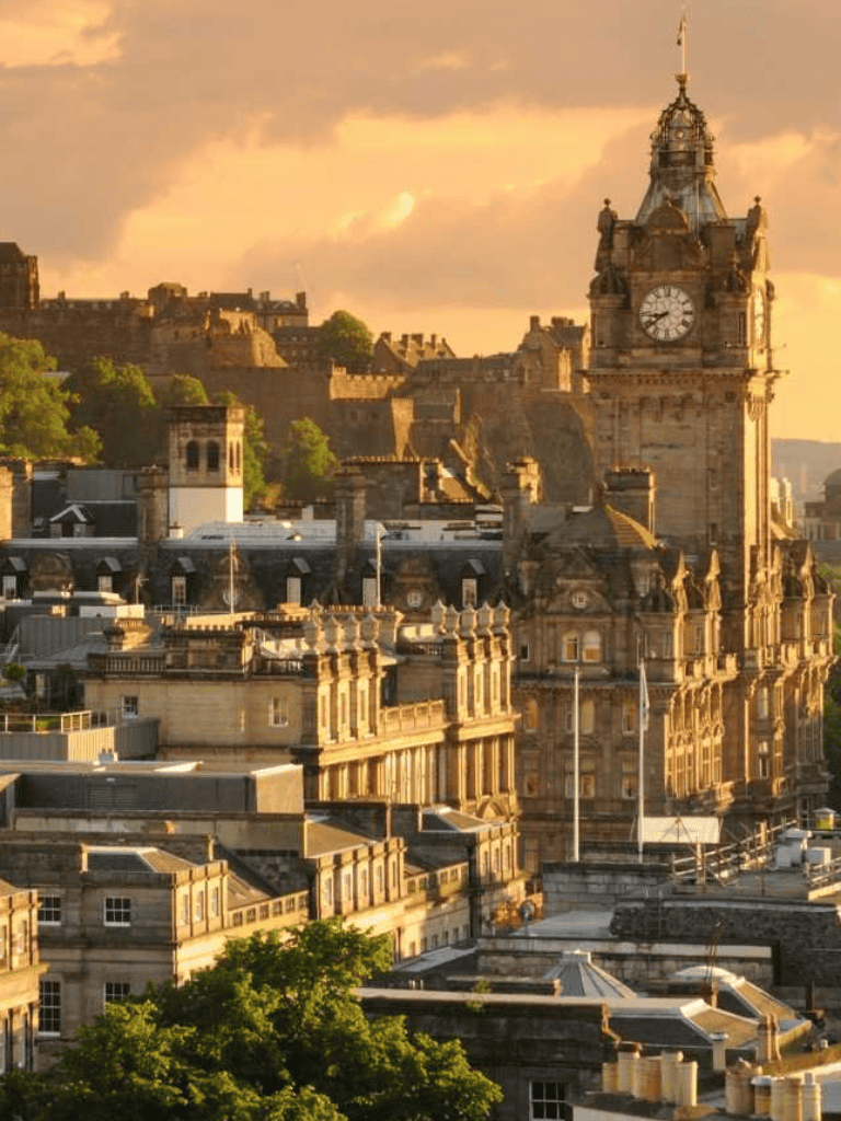 Ancient cityscape with historic buildings and clock tower at sunset, showcasing Edinburgh's architecture and scenic beauty.