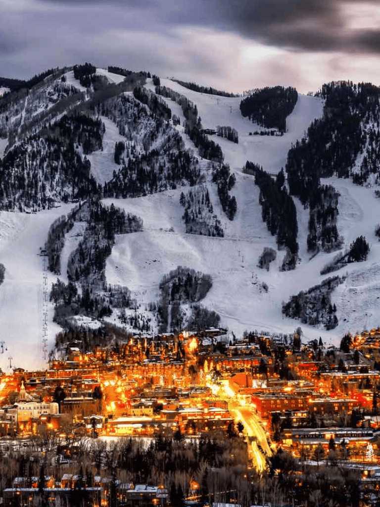 Snowy mountain landscape with ski slopes and a vibrant city illuminated at night, showcasing outdoor winter recreation and urban nightlife.