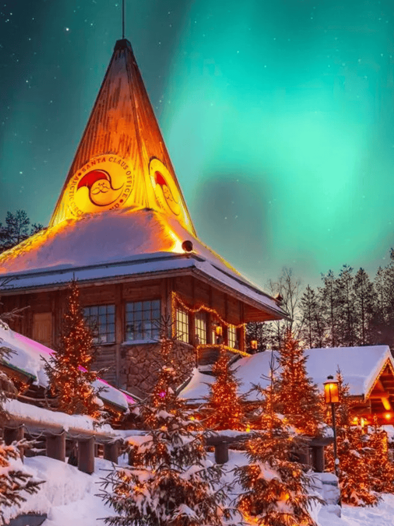 Snowy winter scene at Santa's Lodge with illuminated Christmas trees, cozy chalet, and Northern Lights in the background.