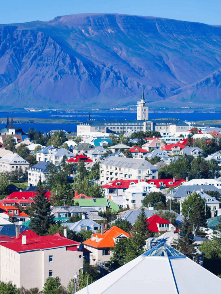 Colorful Icelandic town with mountains and iconic church steeples, vibrant rooftops, scenic landscape, and natural beauty.