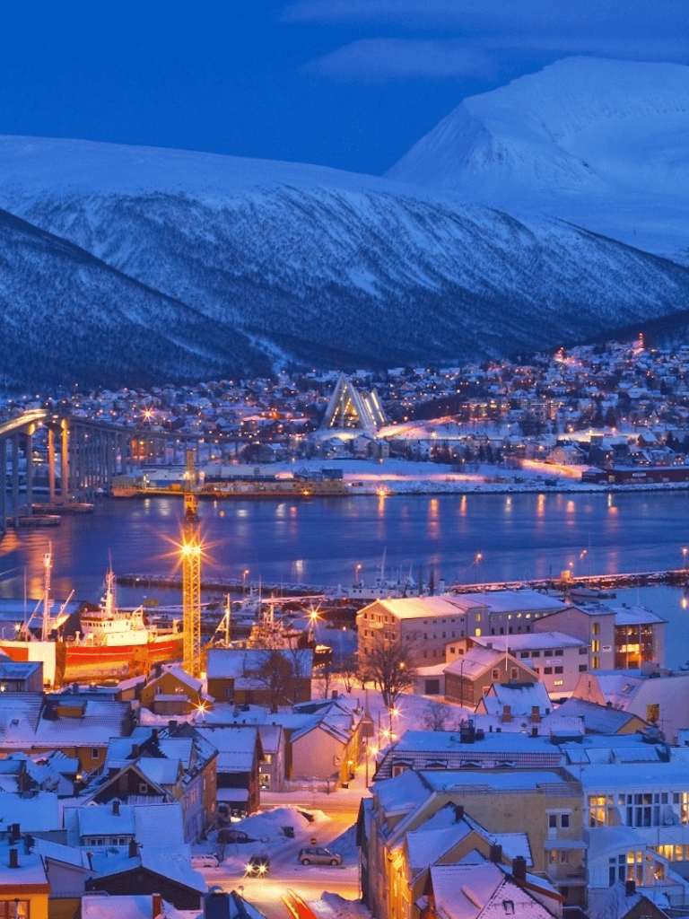 Snowy Arctic townscape with mountains, bridge, and colorful houses at dusk, inspiring winter travel and adventure.