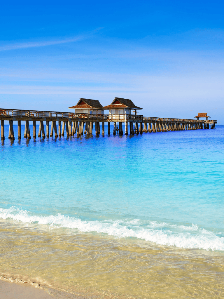 Relaxing tropical beach with wooden pier and huts, clear blue water, sunny sky, ideal for vacation and travel destinations.